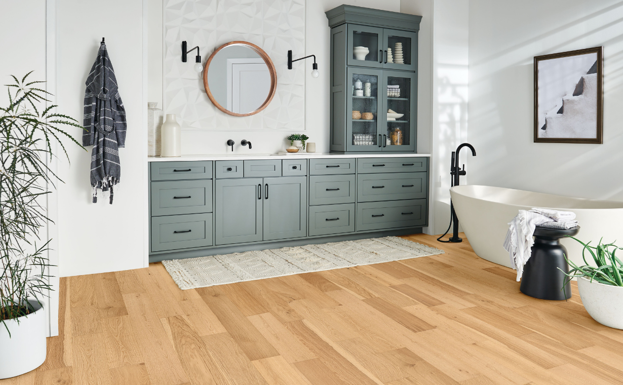 light waterproof hardwood flooring in bathroom with gray cabinets and white soaker tub